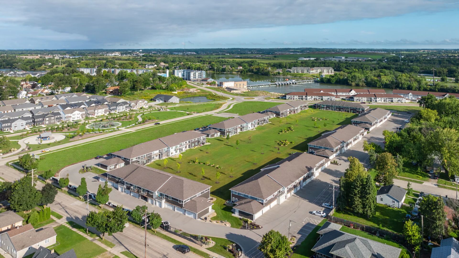 Aerial view of Kimberly Roots: two-story buildings with attached garages around the community green space, Treaty Park at left, the Fox River and the Kimberly dam beyond